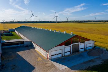 Tuff Rib metal roof on a long farm building beside a field, wind turbines behind