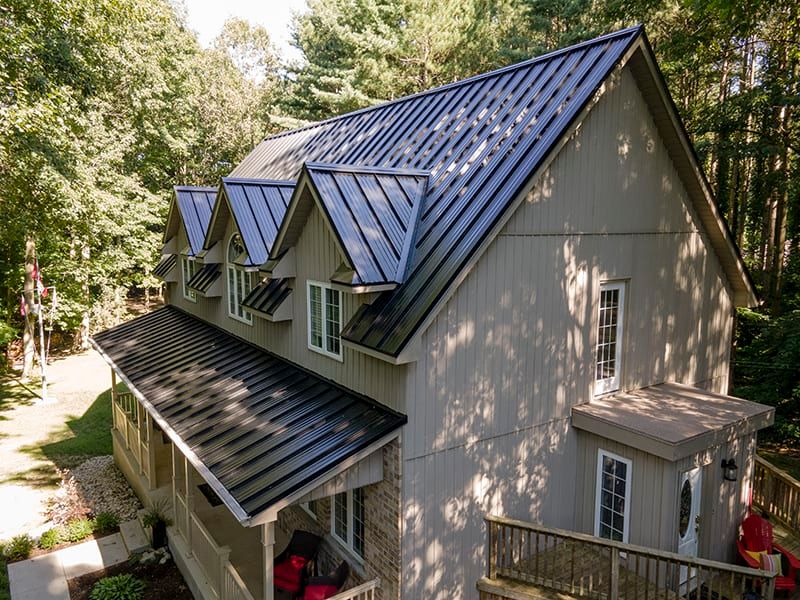 House with a dark standing seam metal roof and dormers among trees